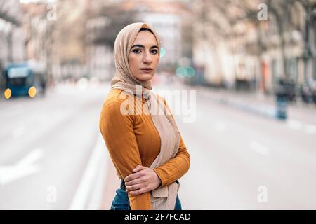 Schöne junge muslimische Frau, die in Hijab auf der Straße steht und die Kamera anschaut. Stockfoto