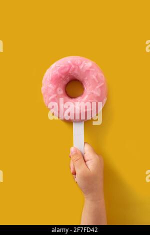 Hand hält einen Erdbeerdonut-Popsicle auf gelbem Hintergrund Stockfoto