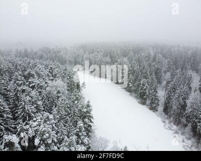 Luftaufnahme des gefrorenen Flusses im Winterwald mit verschneiten Bäumen. Winterlandschaft, Luftlandschaft mit Fluss und Bäumen bedeckt weißen Schnee Stockfoto