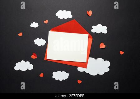 Valentinstag Grußkarte Mockup mit Papier Dekorationen auf schwarzem Hintergrund. Leere Grußkarte oder Einladung und weiße Papierwolken, roter Umschlag Stockfoto
