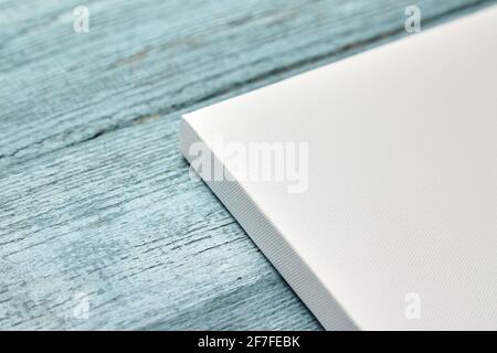 Weiße Leinwand an hellblauer Holzwand. Ecke der leeren Leinwand auf der Trage Bar gestreckt, Seitenansicht, Nahaufnahme Stockfoto