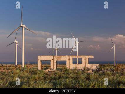 Die Ruinen einer Farm der Sowjetzeit gegen die Hintergrund moderner Windenergieanlagen Stockfoto