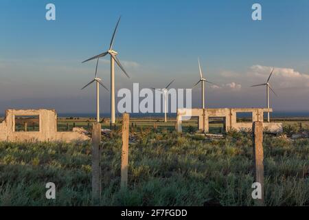 Die Ruinen einer Farm der Sowjetzeit gegen die Hintergrund moderner Windenergieanlagen Stockfoto