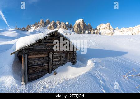 Vereinzelte Holzhütte mit Schnee bedeckt mit Zirnspitzen im Hintergrund bei Sonnenuntergang, Grödnerjoch, Dolomiten, Südtirol, Italien, Europa Stockfoto