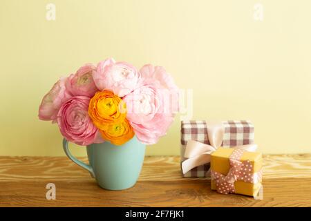 Geschenkboxen und Vase mit Ranunculus-Blumen auf Holztisch. Gelber Hintergrund Stockfoto
