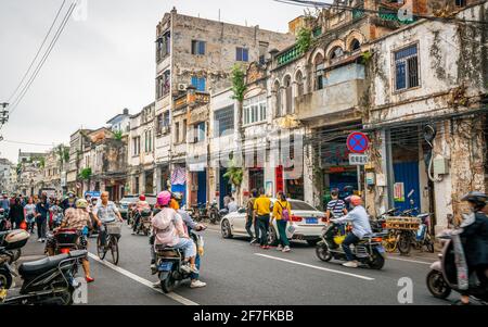 Haikou China , 21 March 2021 : Straßenansicht der Haikou Altstadt mit alten heruntergefahrenen Gebäuden und überfüllten Boai Nordstraße mit Menschen und Motorroller in Stockfoto