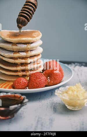 Heiße Pfannkuchen mit Honig auf einem Teller. Leckeres Gericht zum Frühstück. Honig fließt von einem Holzstock auf eine Schüssel. Hausgemachtes Essen Stockfoto