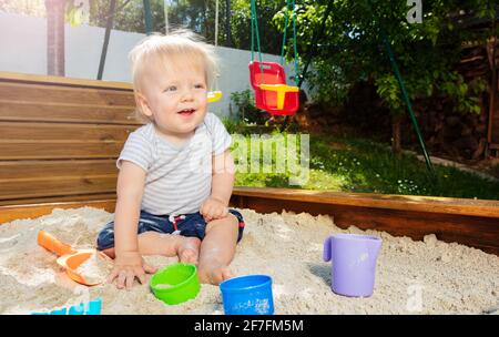 Hübscher blonder Junge spielt im Sandkasten lächelnd Stockfoto