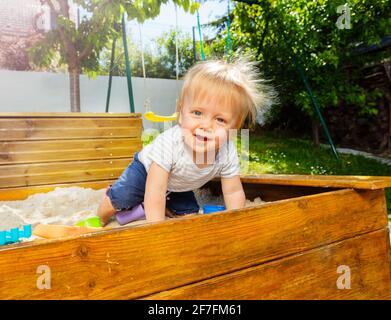 Niedliche kleine blonde Junge sitzen und spielen in Sandbox Stockfoto