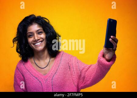 Schöne Sri Lanka Mädchen macht Technologie Posen mit gelb hell Hintergrund - Junge Frau nutzt Handy lächelnd zu nehmen Fotos Stockfoto