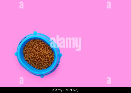 Volle blaue Schale mit Katzenfutter auf einem rosa Hintergrund. Speicherplatz kopieren. Stockfoto