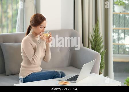 Genießen Sie das Wochenende. Asiatische Mädchen entspannen, Kaffee trinken und mit Laptop, sitzen auf der Couch zu Hause Stockfoto