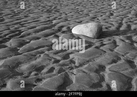 Ein Felsen am Strand zwischen Wellen im Sand, die durch die zurücktretende Flut verursacht werden. Stockfoto