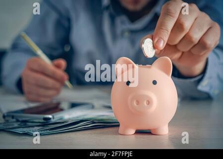 Sparkonzept. Mann Hand Putting Coin Drop in Sparschwein und Buchhaltung berechnen Smartphone-Ausgaben mit Spargeld Münzen, sparen Geld con Stockfoto