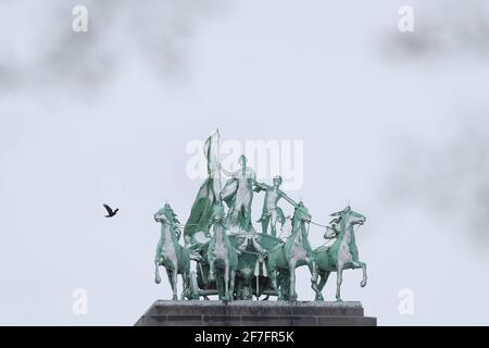 Brüssel, Belgien. April 2021. Ein Vogel fliegt an den schneebedeckten Statuen im Cinquantenaire Park in Brüssel, Belgien, am 7. April 2021 vorbei. In den letzten Tagen trifft seltener Schneefall im April Belgien. Quelle: Zheng Huansong/Xinhua/Alamy Live News Stockfoto