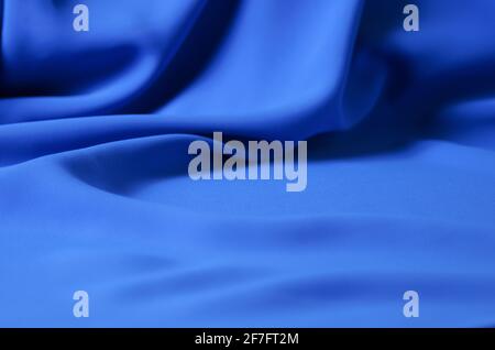 Der unscharfe, unscharfe Hintergrund besteht aus einem zarten blauen Chiffon-Stoff mit Falten in Form von Wellen. Selektiver Fokus. Stockfoto