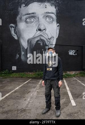 Der Straßenkünstler Akse steht vor seinem Wandbild von Joy Divisons Frontmann Ian Curtis. Stockfoto