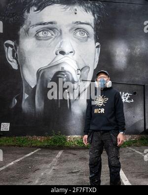 Der Straßenkünstler Akse steht vor seinem Wandbild von Joy Divisons Frontmann Ian Curtis. Stockfoto