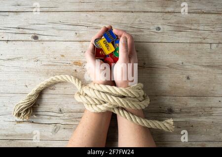 Die Hände des Menschen sind mit einem Seil gebunden und in seinen Händen hält er Token, Chips, Konzept sucht, Glücksspiel sucht Stockfoto