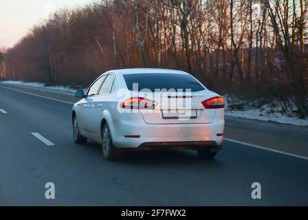 Weißes Auto bewegt sich im Winter auf einer Landstraße Stockfoto