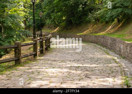 Ein gepflasterter Steinweg, der vom Berg hinunter führt. Steinweg und Mauer. Holzzaun aus dicken Balken. Stockfoto