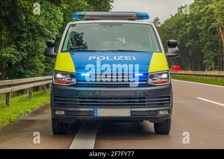 Vorderansicht eines Polizeiautos auf der Autobahn. Zweispurige Autobahn bei regnerischem Wetter. Aktiviertes blaues Licht und Scheinwerfer im vorderen Bereich. Schutzschienen Stockfoto