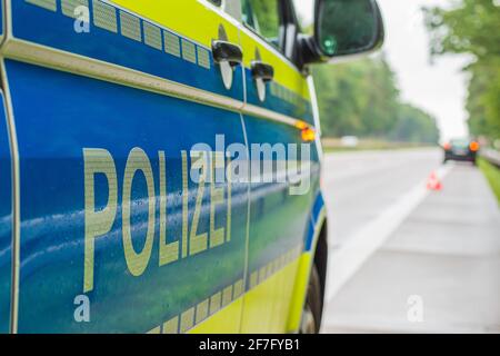 Blick an einem deutschen Polizeiwagen auf der Autobahn vorbei. Schriftzug auf dem Body mit reflektierenden Streifen auf blauem und gelbem Hintergrund. Verregnete Gassen und Bäume. Stockfoto
