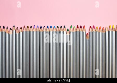Buntstifte, die in einer Reihe auf einem rosa Hintergrund aufgereiht sind, sind das Thema Kreativität und Hobby. Stockfoto