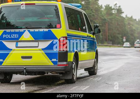 Polizeiauto auf der Autobahn im Land Brandenburg. Asphaltierte Straßenoberfläche bei Regenwetter. Abgewinkelte Ansicht des Fahrzeugs von hinten. Gelbblau Stockfoto