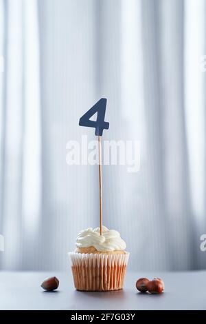 Geburtstagskuchen oder Muffin mit Nummer 4 vier und Haselnüssen auf dem Tisch und hellem Hintergrund. Geburtstag oder Jubiläum Grußkarte Konzept. Hochwertige vertikale Fotos Stockfoto