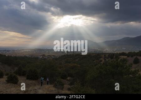 Sonnenstrahlen brechen durch die Wolken über einem Meer und Berge Stockfoto