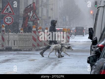 München, Deutschland. April 2021. Eine Frau mit einem Hund überquert im Bezirk Schwabing eine Straße im Schnee. Kredit: Peter Kneffel/dpa/Alamy Live Nachrichten Stockfoto