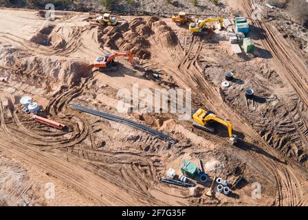 Installation von Sturmwasserkanälen und Bau einer Straße in einem neuen Wohngebiet. Bagger auf Erdarbeiten, Blick von oben, Blick von der Drohne. Ro Stockfoto