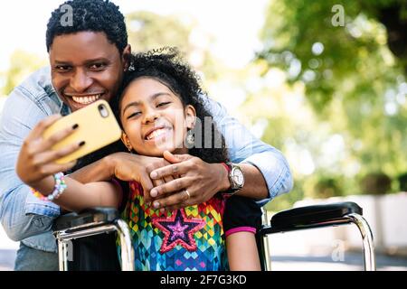 Mädchen im Rollstuhl und ihr Vater machen ein Selfie mit dem Telefon. Stockfoto