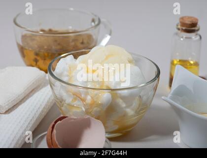 Inhaltsstoffe der Maske „Eierweiß“. Geschlagenes Eiweiß, Mandelöl, Honig, Kamillentee. Hausgemachte Kosmetik. Nahaufnahme. Stockfoto