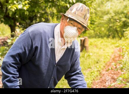 Älterer Mann mit Schutzbrille, Maske und Hut arbeitet im Garten. Stockfoto
