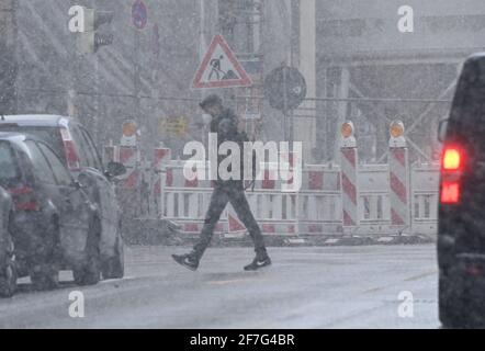 München, Deutschland. April 2021. Ein Mann überquert eine Straße im Stadtteil Schwabing im Schnee. Kredit: Peter Kneffel/dpa/Alamy Live Nachrichten Stockfoto