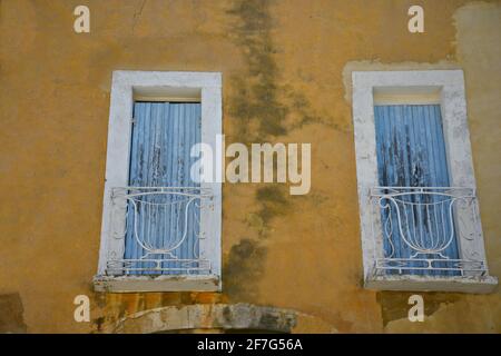 Alte Fassade im Provençal-Stil mit ockerfarbener Wand und blauen Fensterläden im historischen Dorf Ménerbes, Provence-Alpes-Côte d'Azur Vaucluse, Frankreich Stockfoto