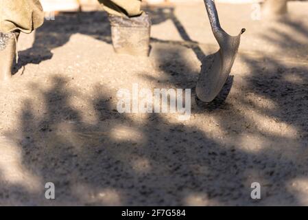 Gießen von Betonplatten. Füße und Schaufel des Arbeiters. Beton mit einem Handwerkzeug ausgleichen. Stockfoto