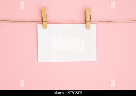 Leeres Papierblatt für Notizen, Rahmen, die an einem Seil mit Wäscheklammer hängen und isoliert auf rosa Hintergrund. Weißes Leerzeichen mit leerem Leerzeichen für Text. Stockfoto