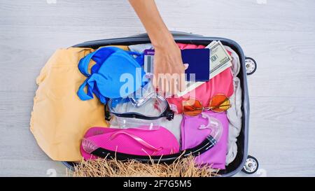 Teilansicht einer Frau, die beim Packen des Koffers ihren Pass einlegt Sommerkleidung zu Hause Stockfoto