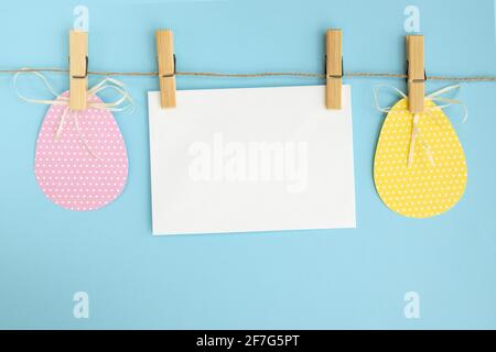Bunte osterkarte und Girlande mit bemalten Eiern auf blauem Hintergrund mit leerer Karte. Bunte Feiertagsdekoration Draufsicht Stockfoto