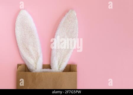 Flauschige Hasenohren in Papiertüte, isoliert auf rosa Hintergrund. Kaninchen. Osterideen. Platz für Text. Einkaufs- und Urlaubskonzept. Stockfoto