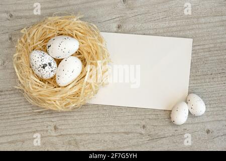 Ostereier in einem Strohnest und Grußkarte über weißem Holz. Vorlage Ostern Grußkarte. Draufsicht mit Kopierbereich. Stockfoto