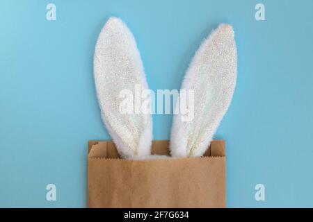 Flauschige Hasenohren in Papiertüte, isoliert auf blauem Hintergrund. Kaninchen. Osterideen. Platz für Text. Einkaufs- und Urlaubskonzept. Stockfoto