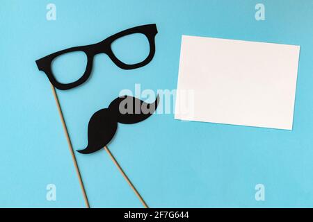 Fröhlicher Vatertag, Komposition aus schwarzem Schnurrbart und Brille auf blauem Hintergrund, Grußkarte mit weißem Blatt Papier und Platz für Text Stockfoto