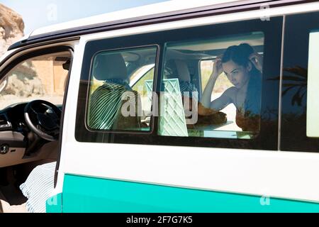 Attraktive Frau in einem Bikini, sieht sich in einem Spiegel, während Kämmen ihre Haare in ihrem Wohnmobil, Road-Trip-Konzept Stockfoto