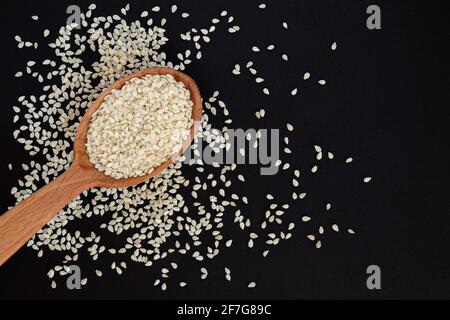 Weiße Sesamsamen in Holzlöffel auf Haufen weißer Sesamsamen, Draufsicht. Stockfoto