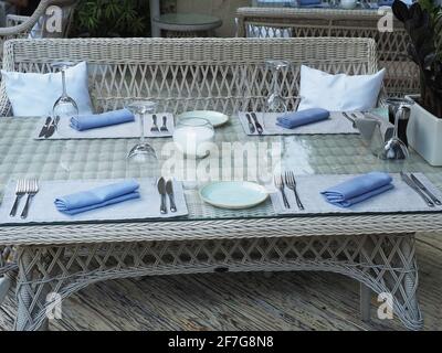 Ein serviertes Rattantisch mit einem Stuhl und Kissen Der Holzboden des Straßencafés Stockfoto