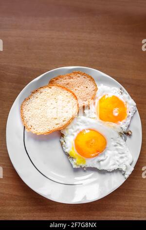 Ein Omelett aus Hühnereiern, frisch zubereitet, steht auf einem Teller und zwei Scheiben Weißbrot. Flaches Layout. Stockfoto